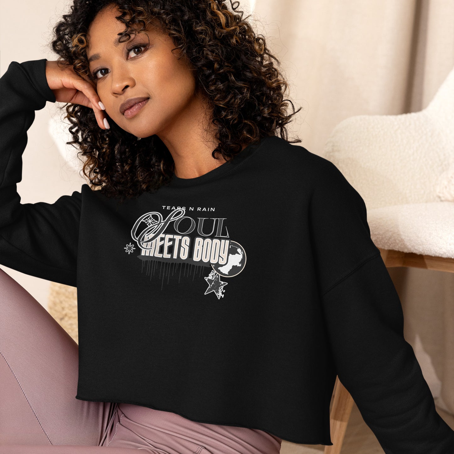 A woman in a black crop top displaying the phrase "be good," standing confidently with a neutral background.