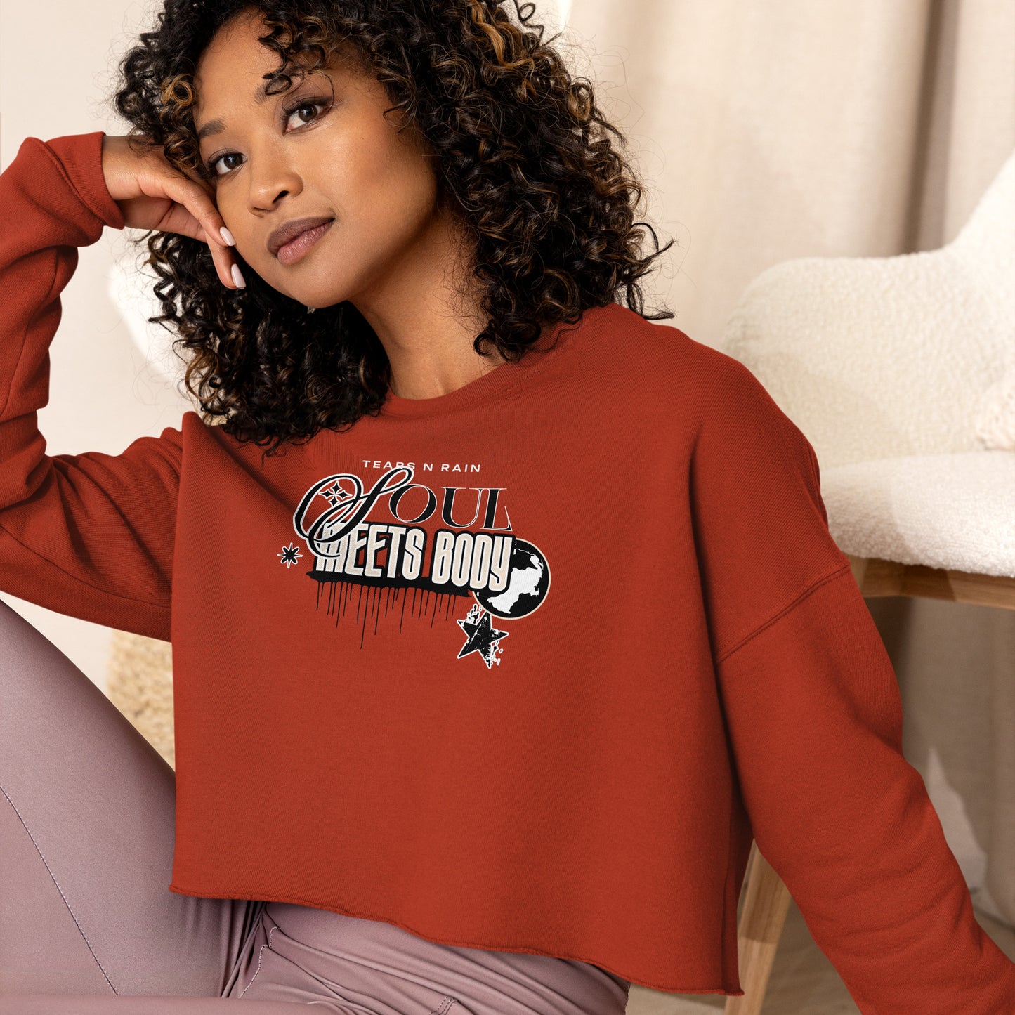 A woman in a red crop top displaying the phrase "be good," standing confidently with a neutral background.