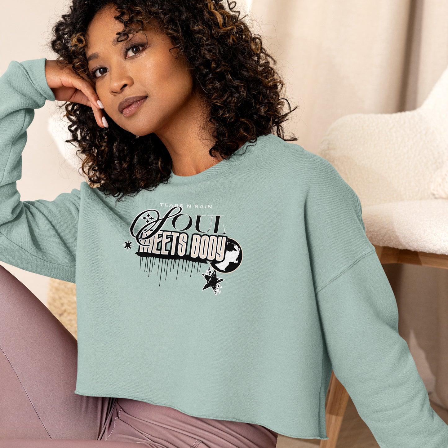 A woman in a blue crop top displaying the phrase "be good," standing confidently with a neutral background.