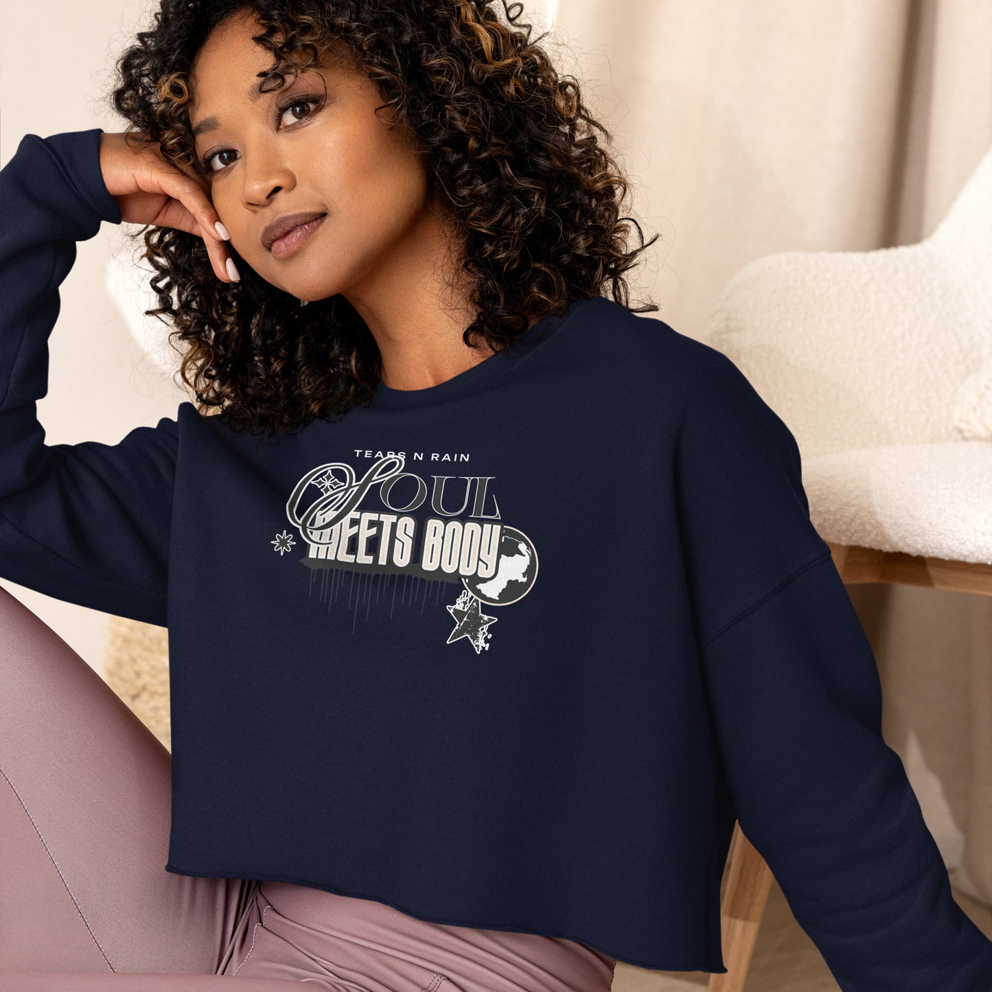 A woman in a navy blue crop top displaying the phrase "be good," standing confidently with a neutral background.